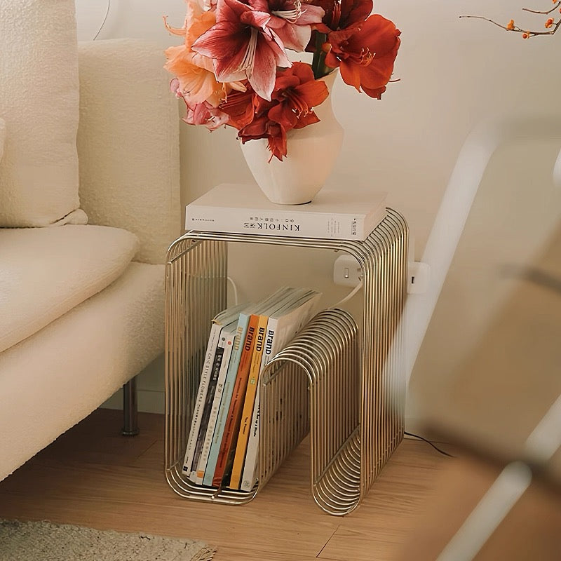 Wire side table with books and a vase of flowers on a wooden floor.