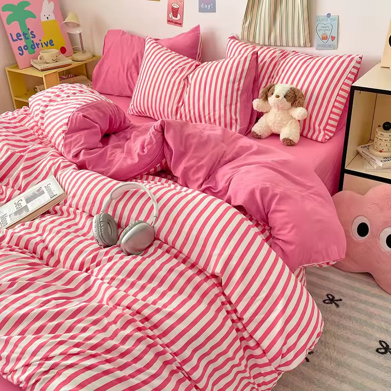 Pink and white striped bedding with a teddy bear and headphones on a bed in a room.