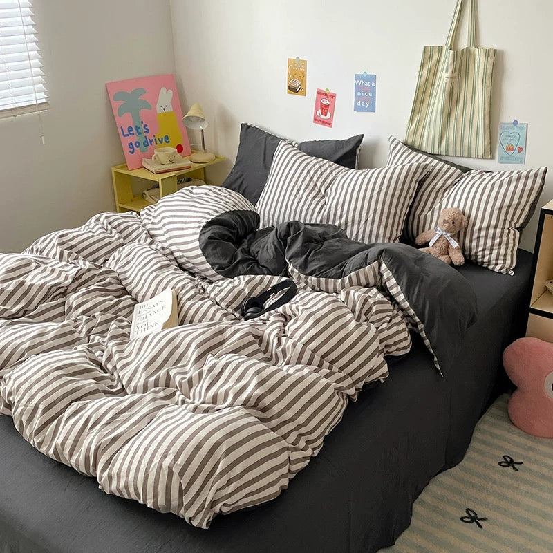 Bed with striped duvet and pillows in a room with a small table and decor items.