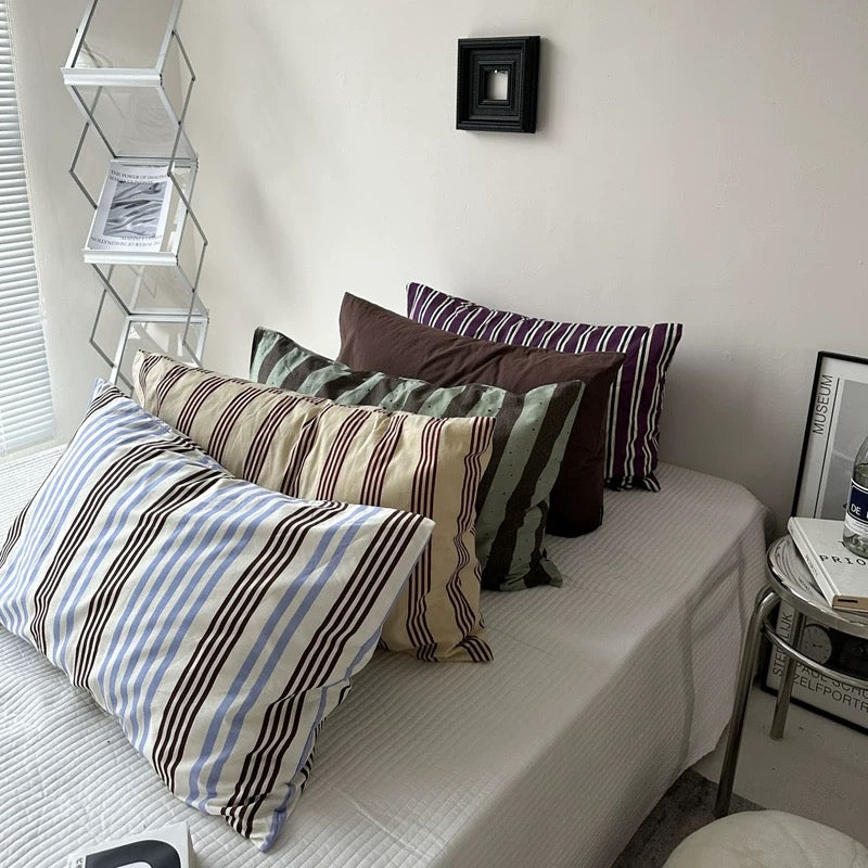 Bed with striped pillows and a small shelf in a room.