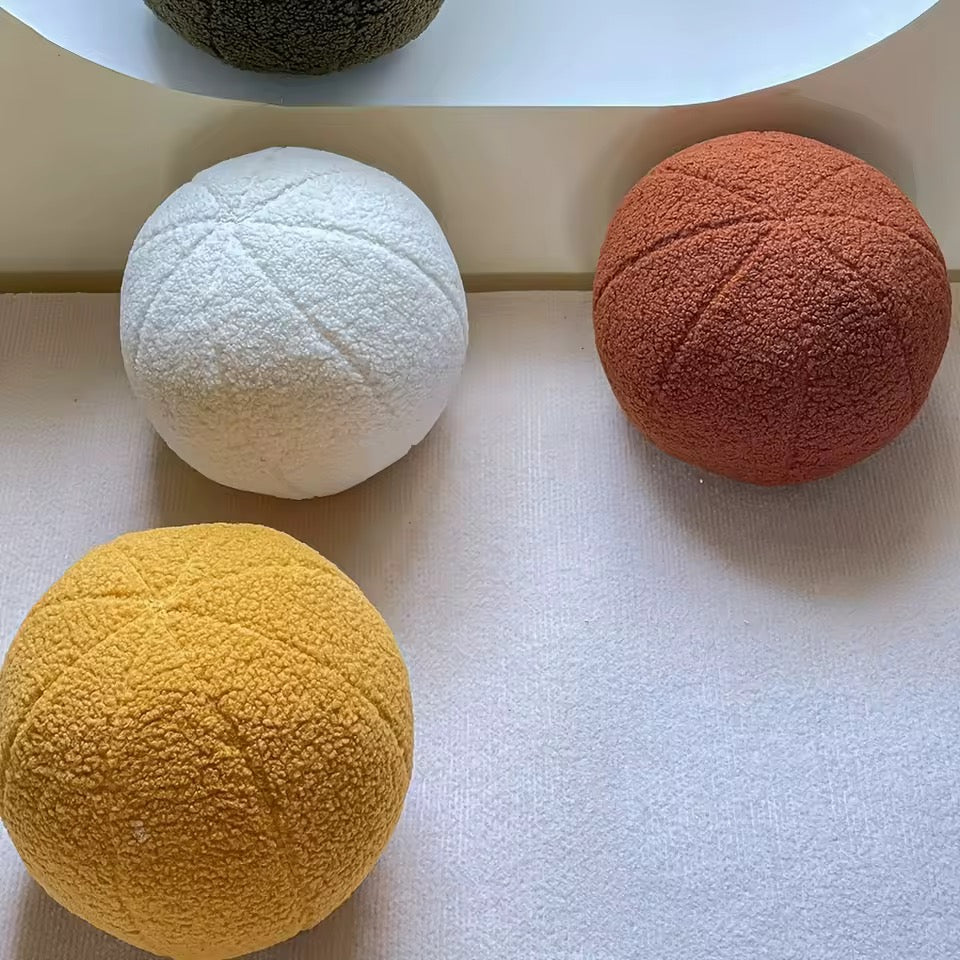 Four textured spherical cushions in green, white, yellow, and orange on a light surface.