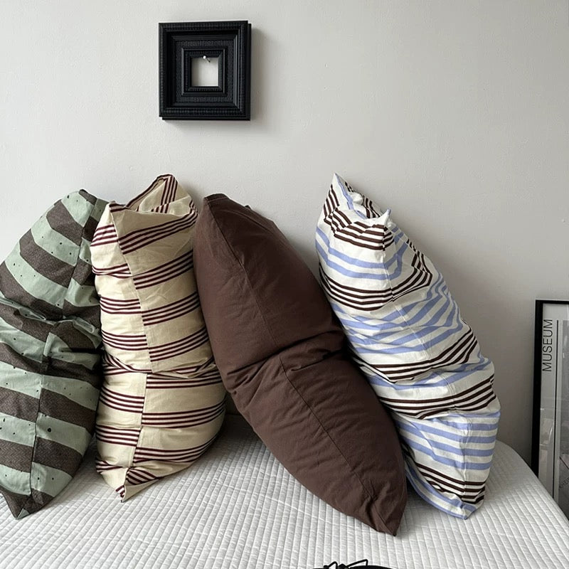 Bed with striped pillows and a small shelf in a room.