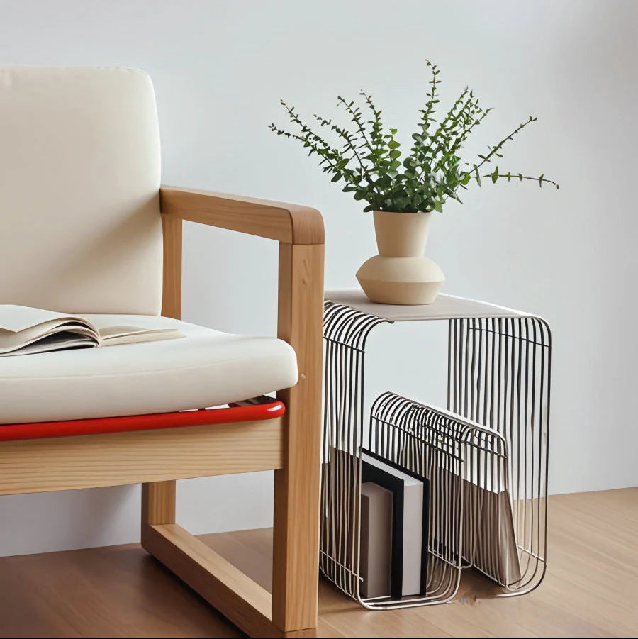 Curved metal table holding books and a Kinfolk magazine beside a soft white armchair