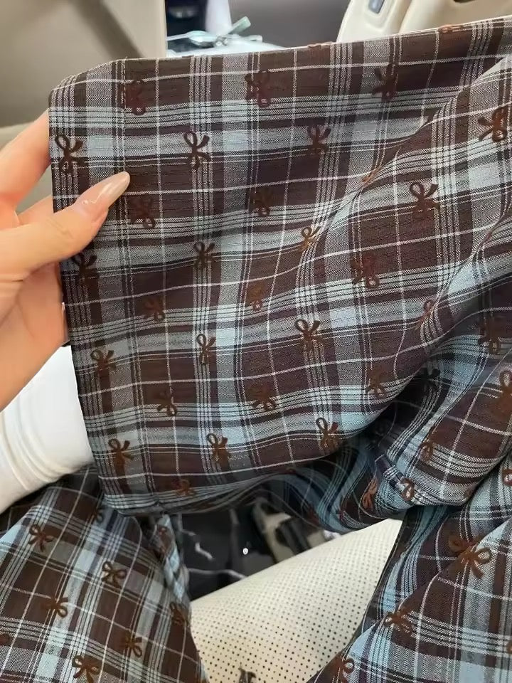 Close-up of plaid fabric with small patterns held by a hand.