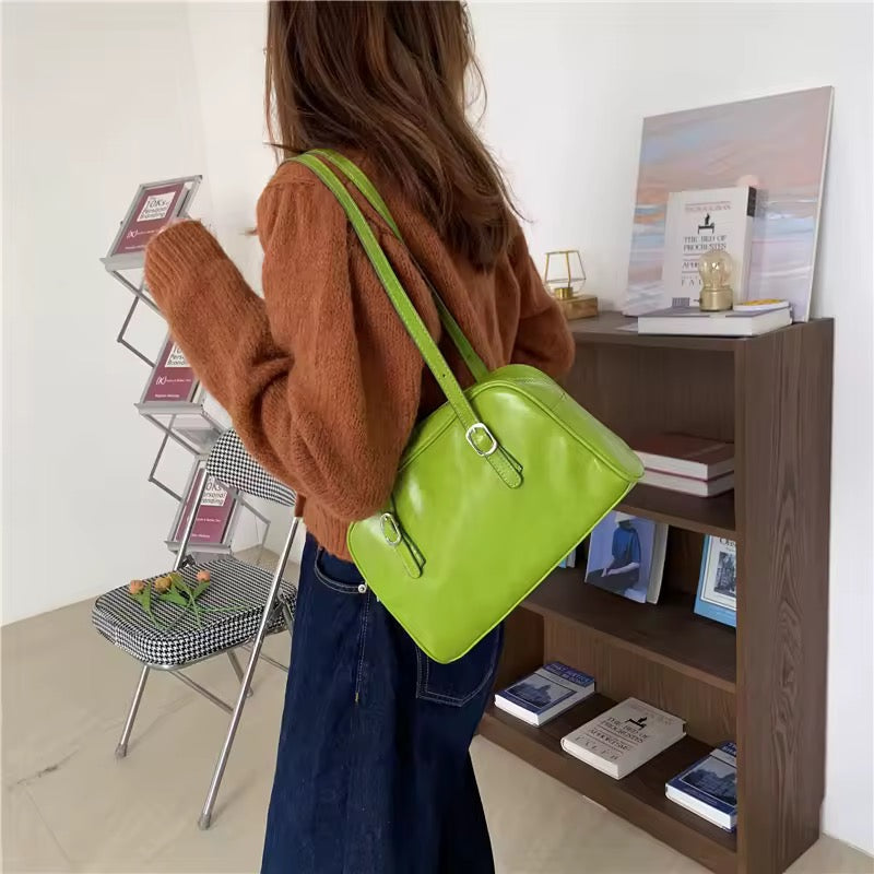 Person holding a green handbag in a room with a bookshelf and chair.