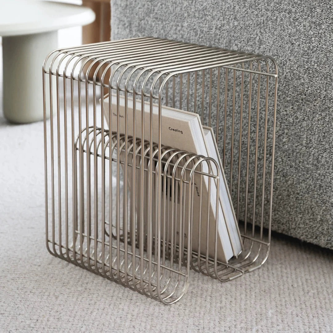 Metal wire magazine rack holding books on a carpeted floor.