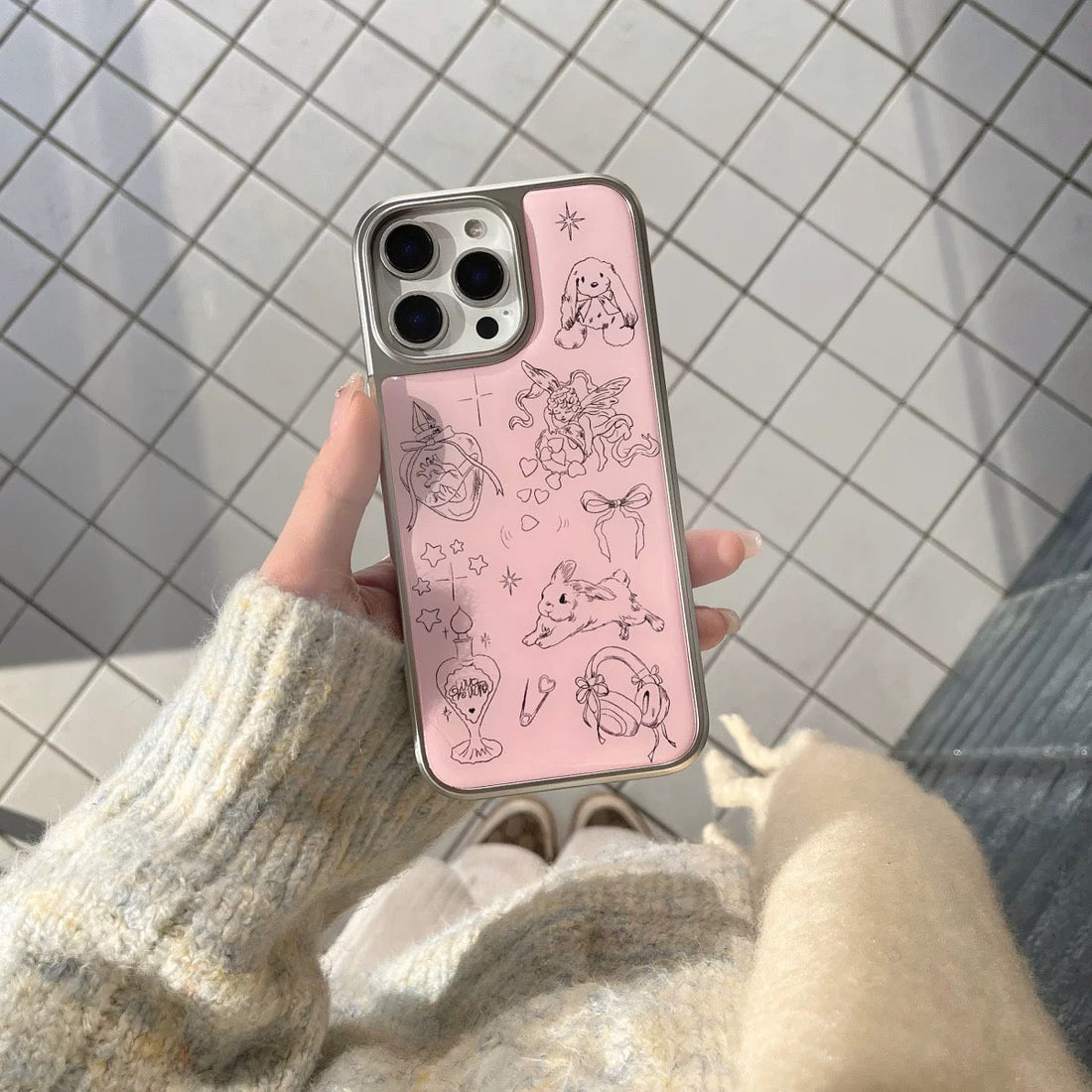 Phone case with cute illustrations held by a person against a tiled wall.