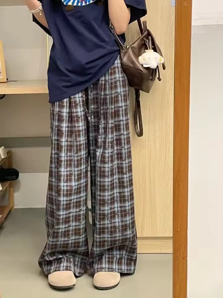 Person wearing plaid pants and a navy top, holding a brown bag indoors.