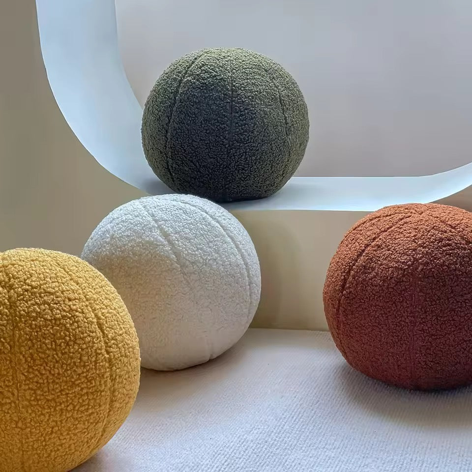 Four textured spherical cushions in green, white, yellow, and orange on a light surface.