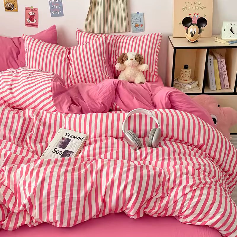 Pink and white striped bedding set with a teddy bear and books on a bed.