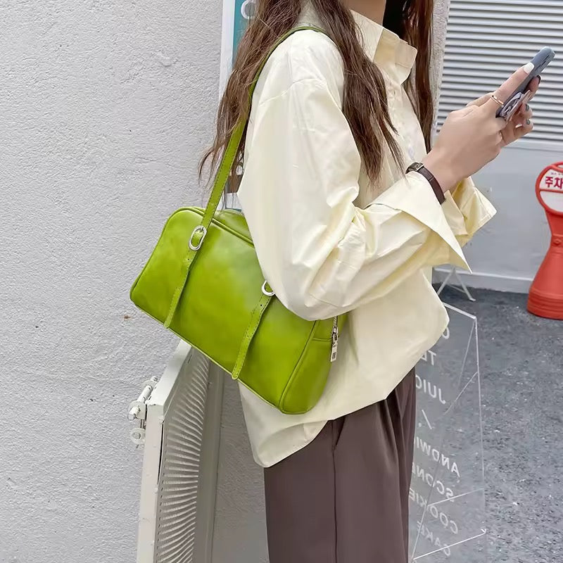 Person holding a green handbag and a phone against a gray wall.
