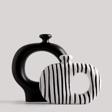 Two ceramic vases, one black and one with black and white striped pattern, on a light gray background.