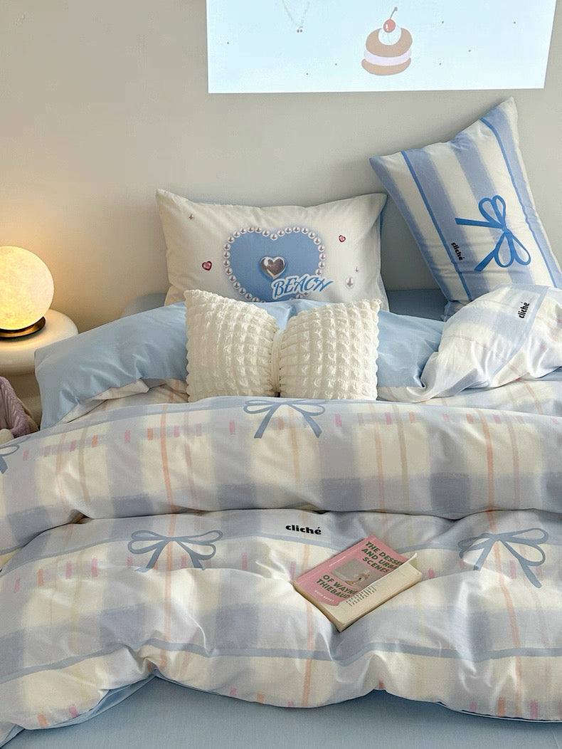Bed with light blue and white checkered bedding, decorative pillows, and a small lamp on a nightstand.