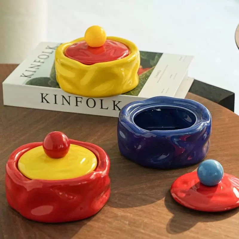 Colorful ceramic containers with lids on a wooden surface, with 'KINFOLK' magazine in the background.