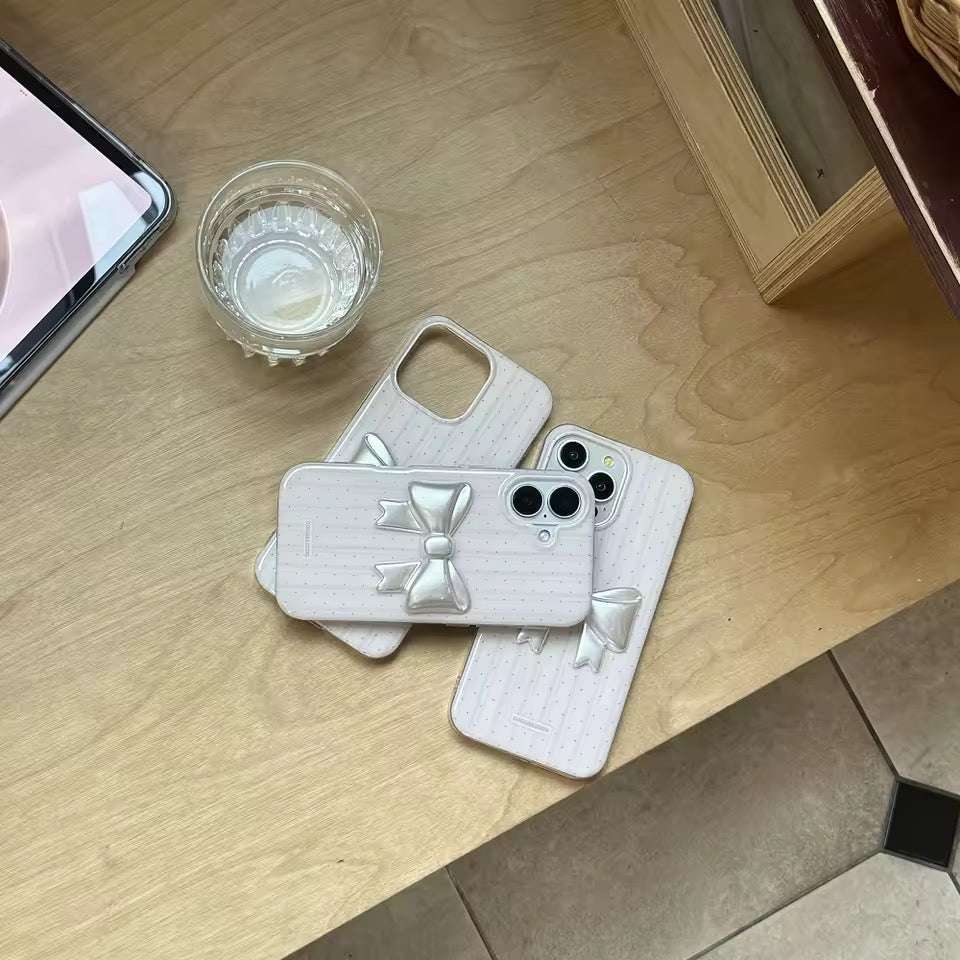 Phone cases with bow design on a wooden surface next to a phone and glass of water.