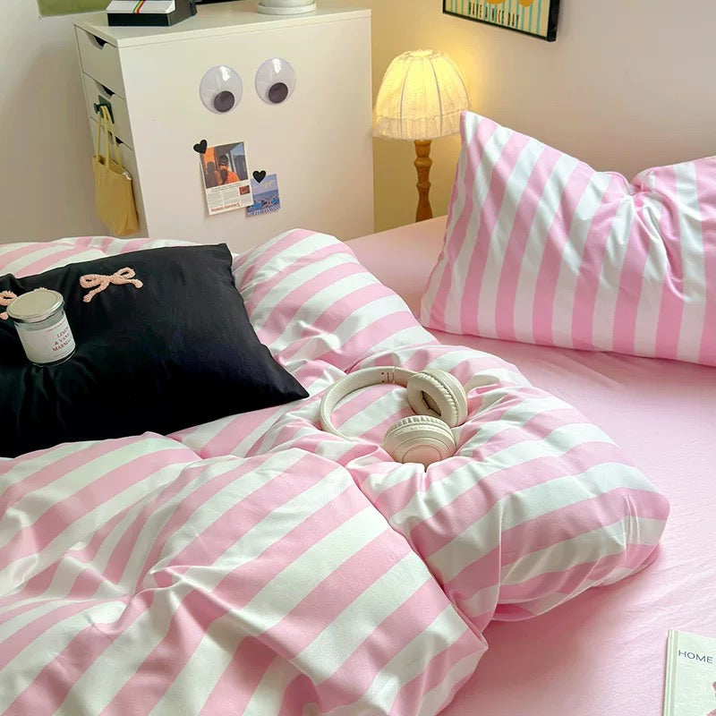 Flat sheet in soft pink tones draped over the bed, coordinating with the striped duvet