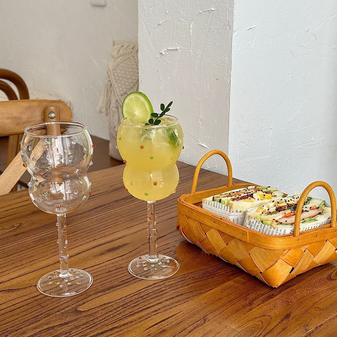 Two glasses with drinks and a basket of snacks on a wooden table.