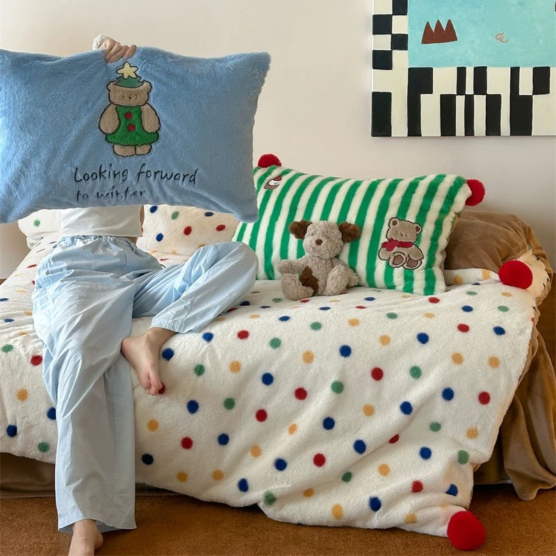 Person lying on a bed with colorful polka dot blanket and pillows featuring teddy bears.