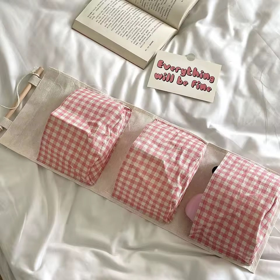 Three pink checkered items in a pouch on a white surface with an open book and a card reading 'Everything will be fine'.