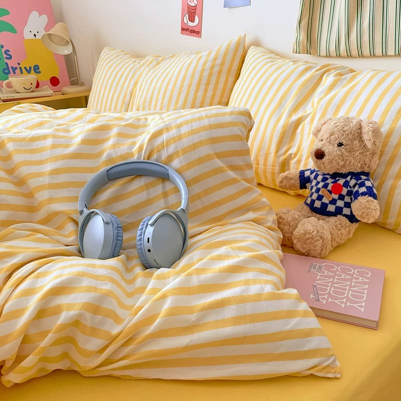 Yellow and white striped bedding with a teddy bear and headphones on a bed.