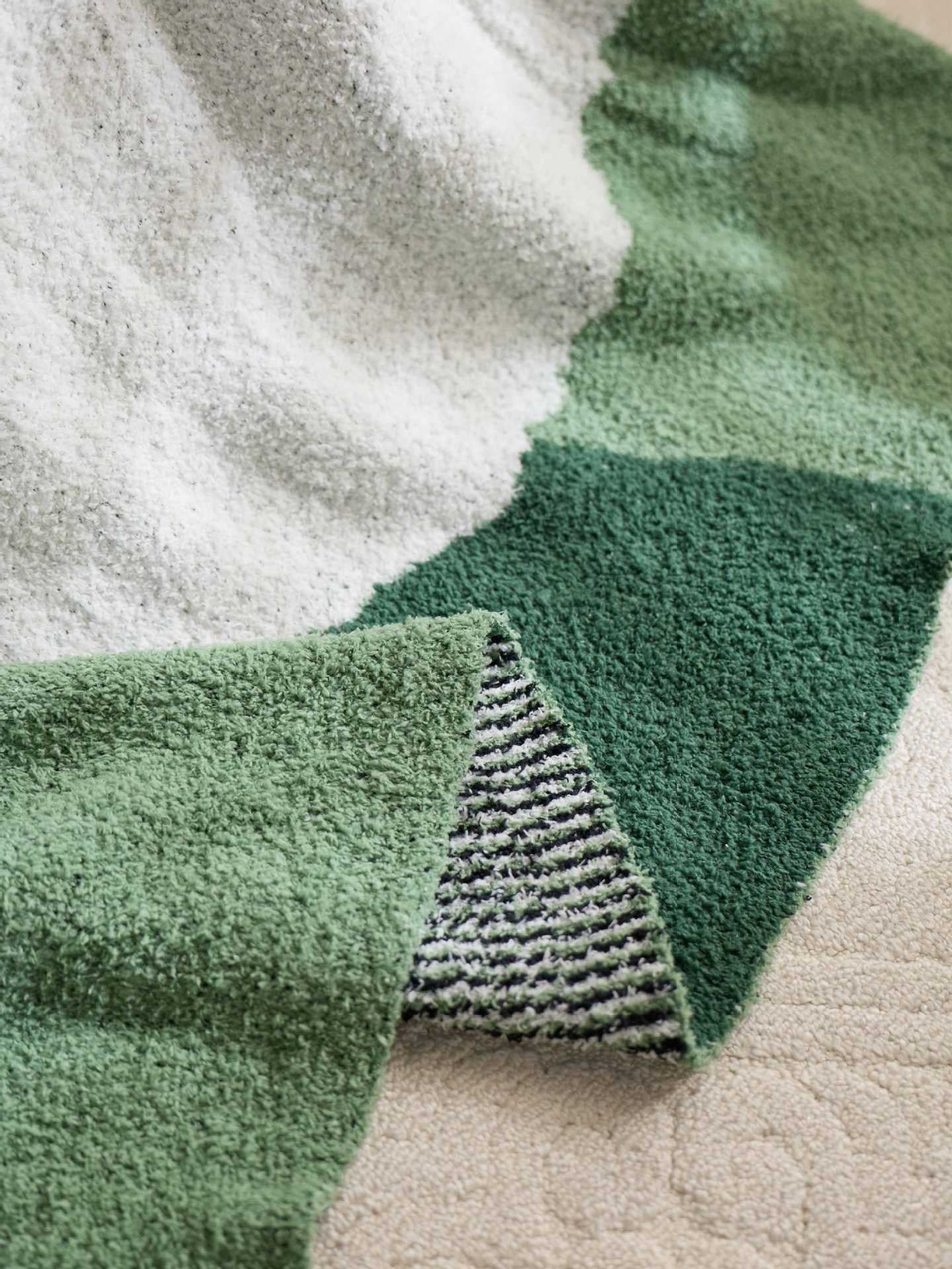 Two white sheep stand across light and dark green areas on a rectangular plush blanket.