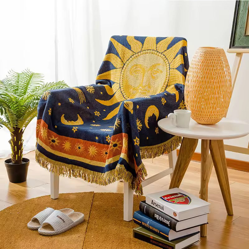 Chair with a sun and moon patterned throw blanket in a room with a plant and books.