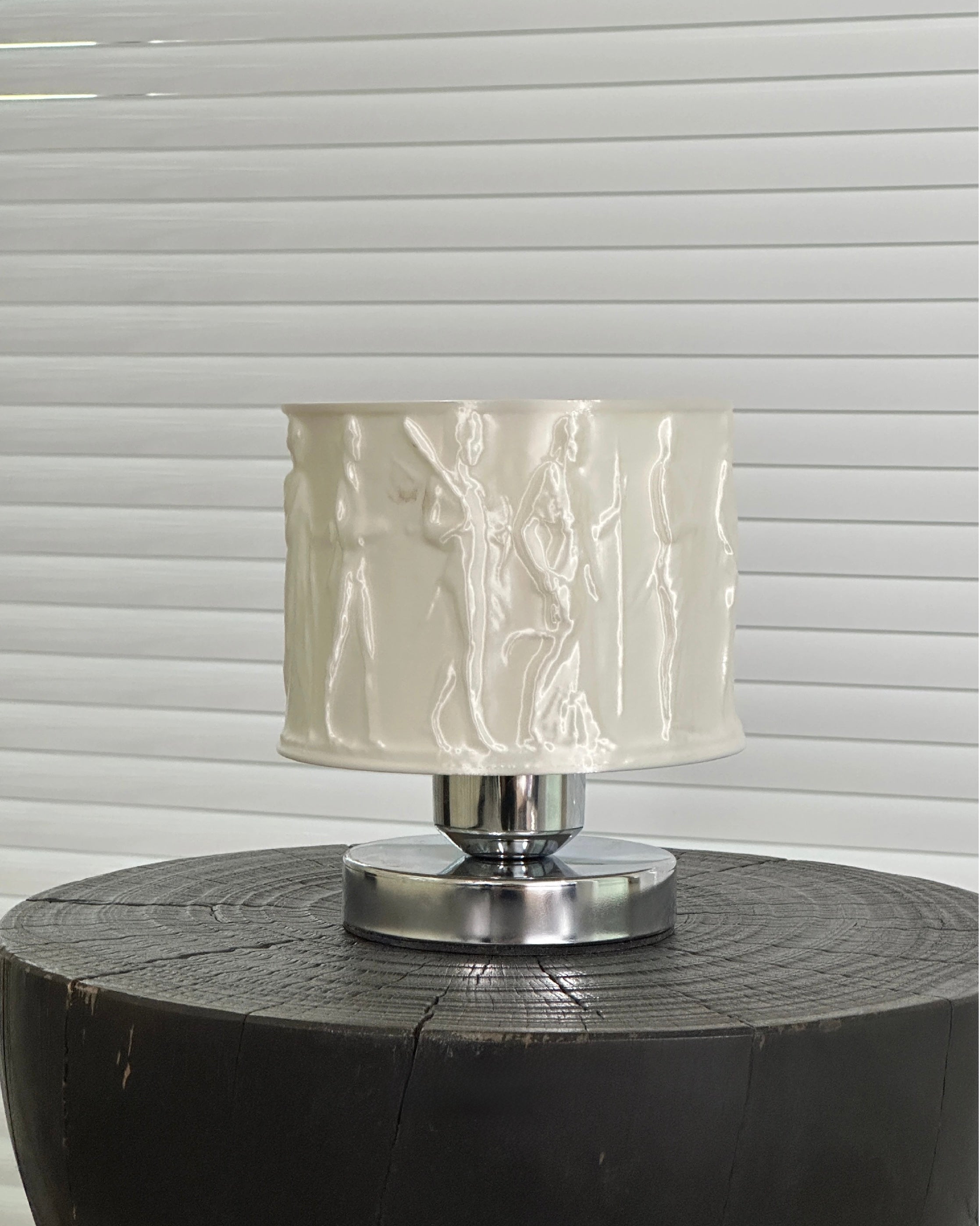 Table lamp with a textured white shade on a wooden base against a window blind background