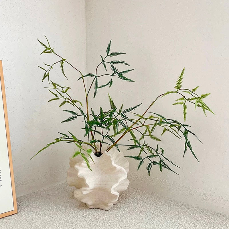 Artificial fern plant in a white shell-shaped vase against a light background