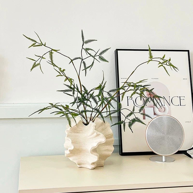 Decorative setup with a shell-shaped vase, plant, and framed poster on a shelf.