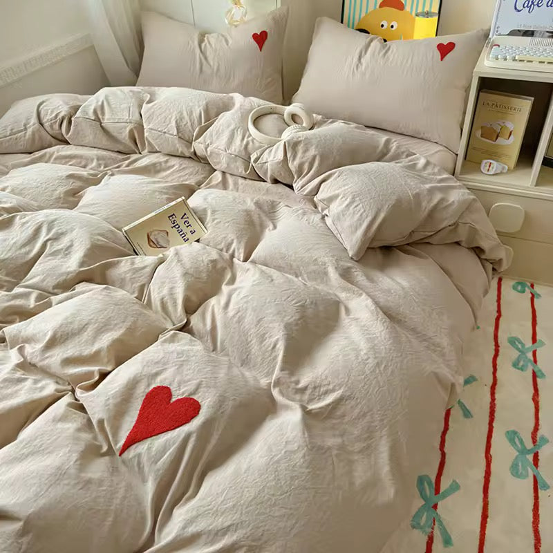 Soft beige bedding set with red embroidered heart on the comforter in a cozy minimalist bedroom
