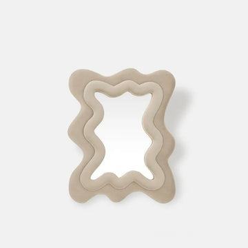 A wavy, layered mirror with a thick, sculptural frame in a matte beige finish, set against a clean, light gray background.