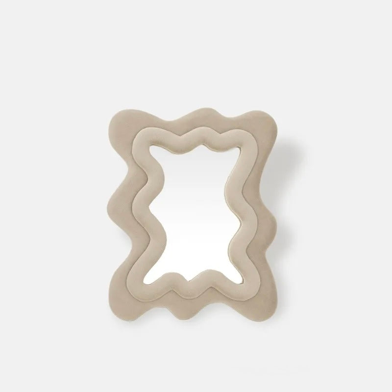 A wavy, layered mirror with a thick, sculptural frame in a matte beige finish, set against a clean, light gray background.