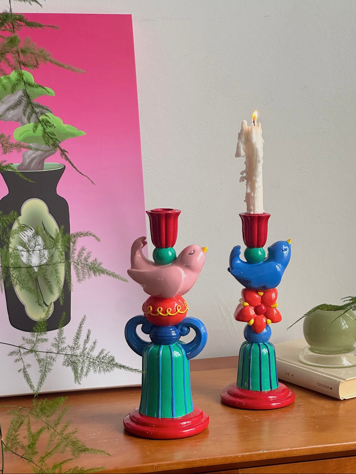Pink and blue bird candle holders displayed together on a round table in front of a pink patterned cushion.
