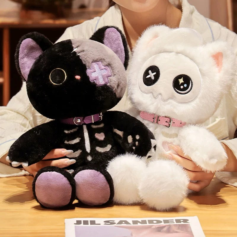 Two plush toys, one black with purple accents and the other white, held by a person on a wooden surface.