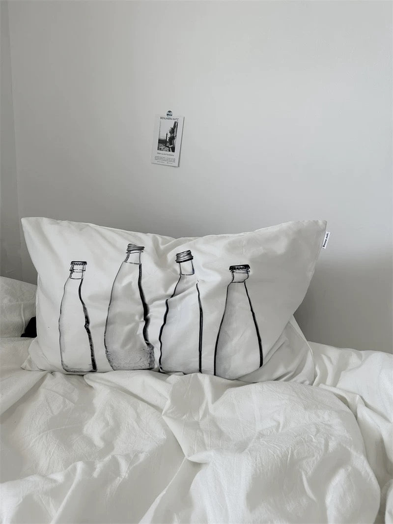 Pillow with bottle design on a bed against a plain wall.