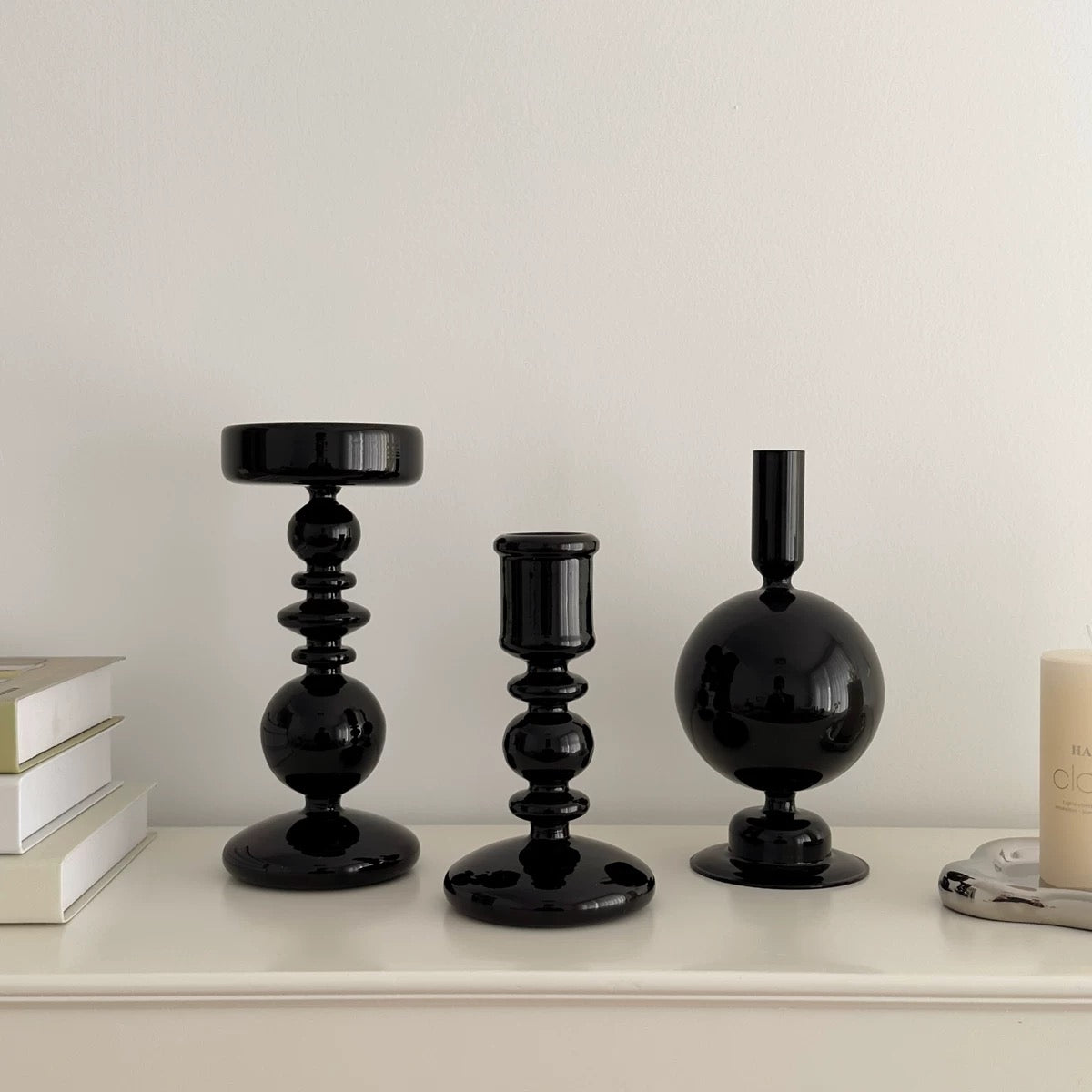 Three black candle holders on a white surface with a neutral background