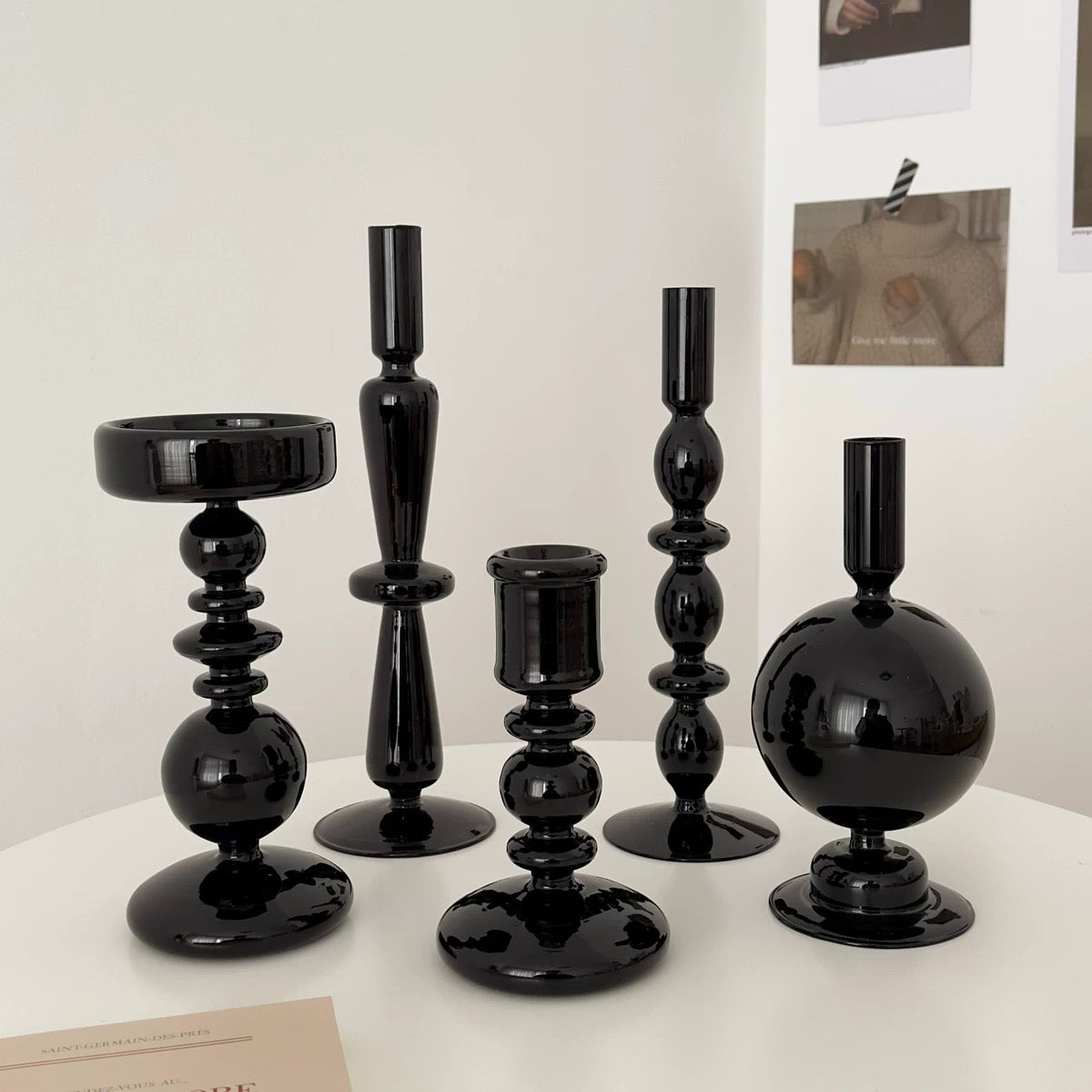 Set of black candle holders on a white surface with a light gray wall in the background.