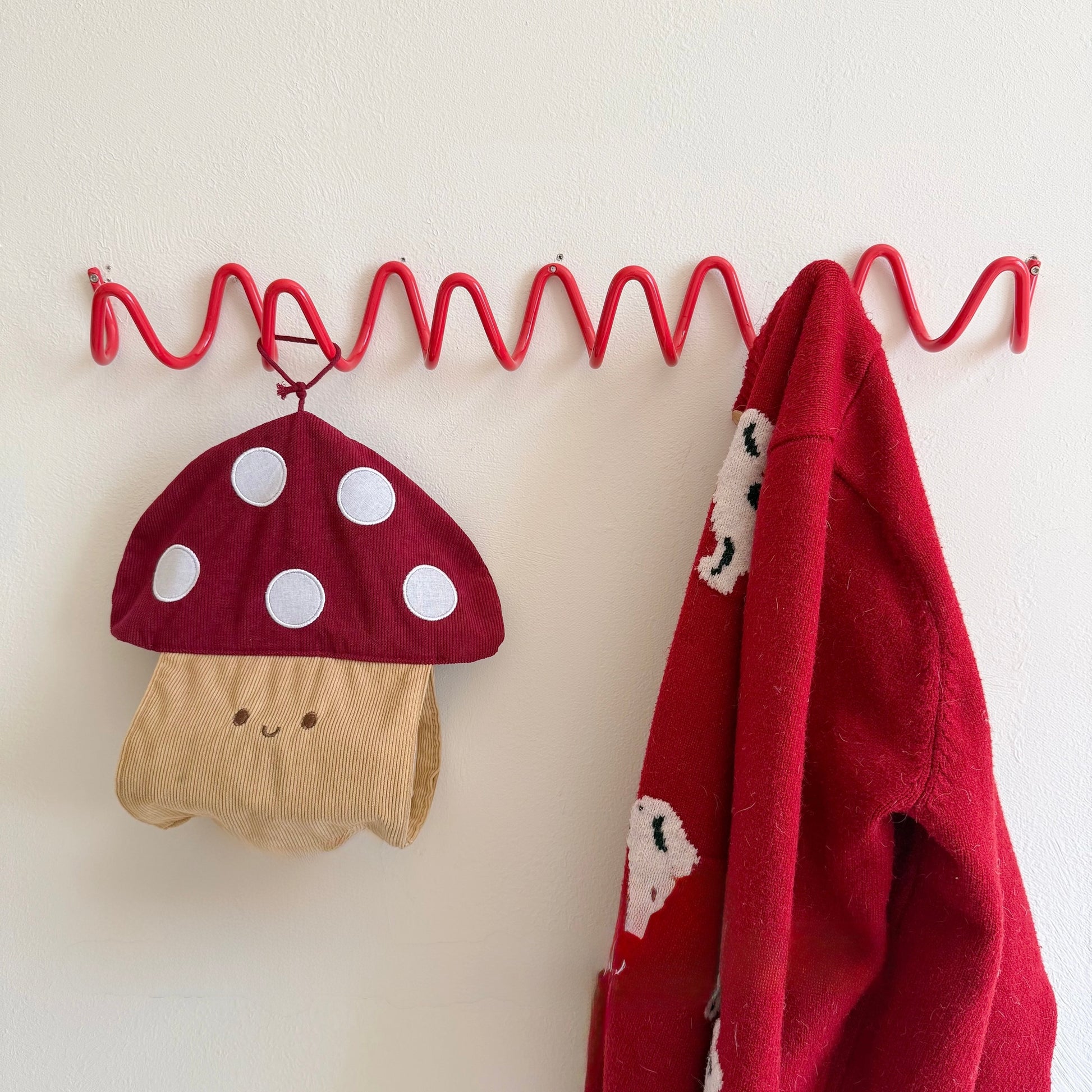 Red mushroom hat and red jacket hanging on a red metal hook against a white wall.
