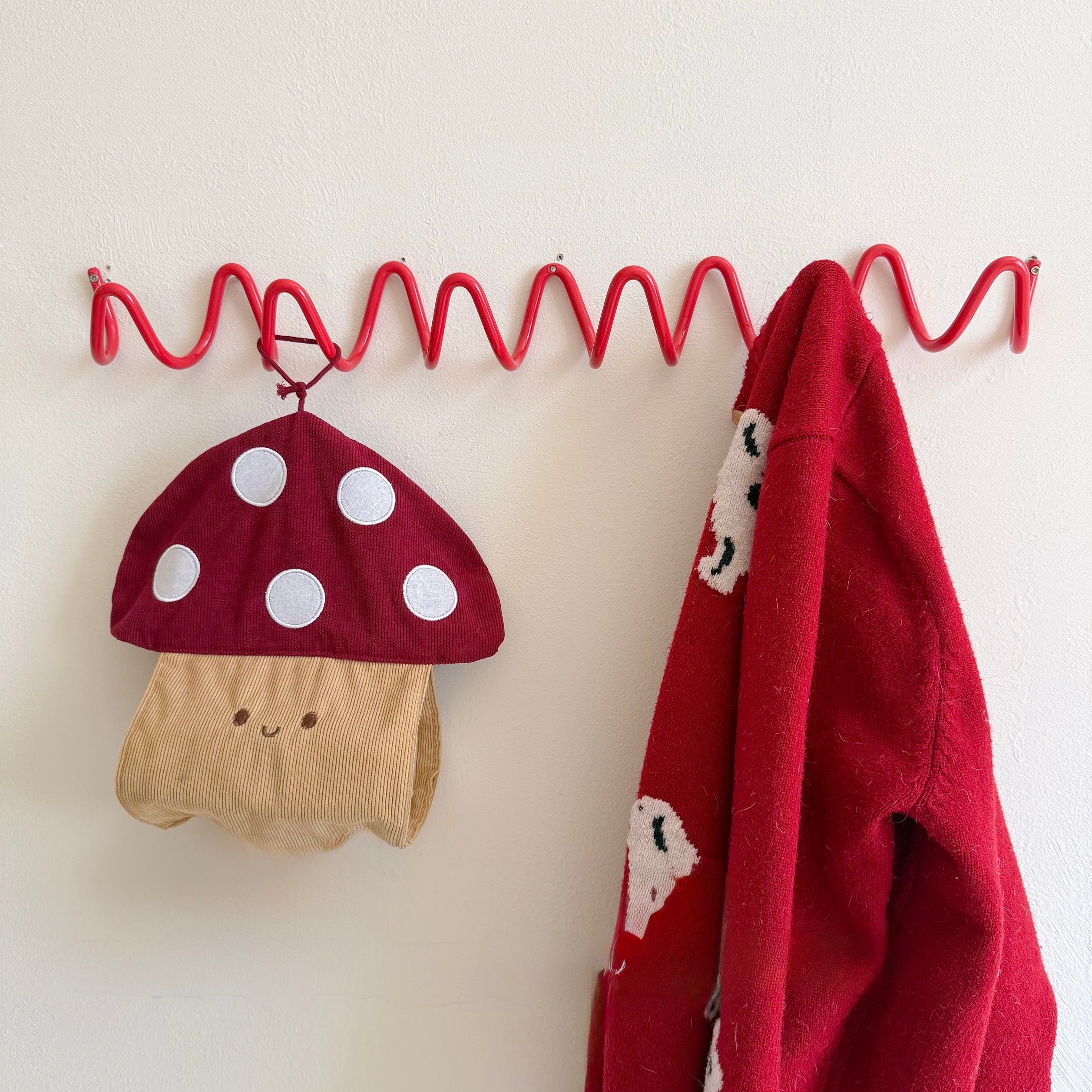 Red mushroom hat and red jacket hanging on a red metal hook against a white wall.