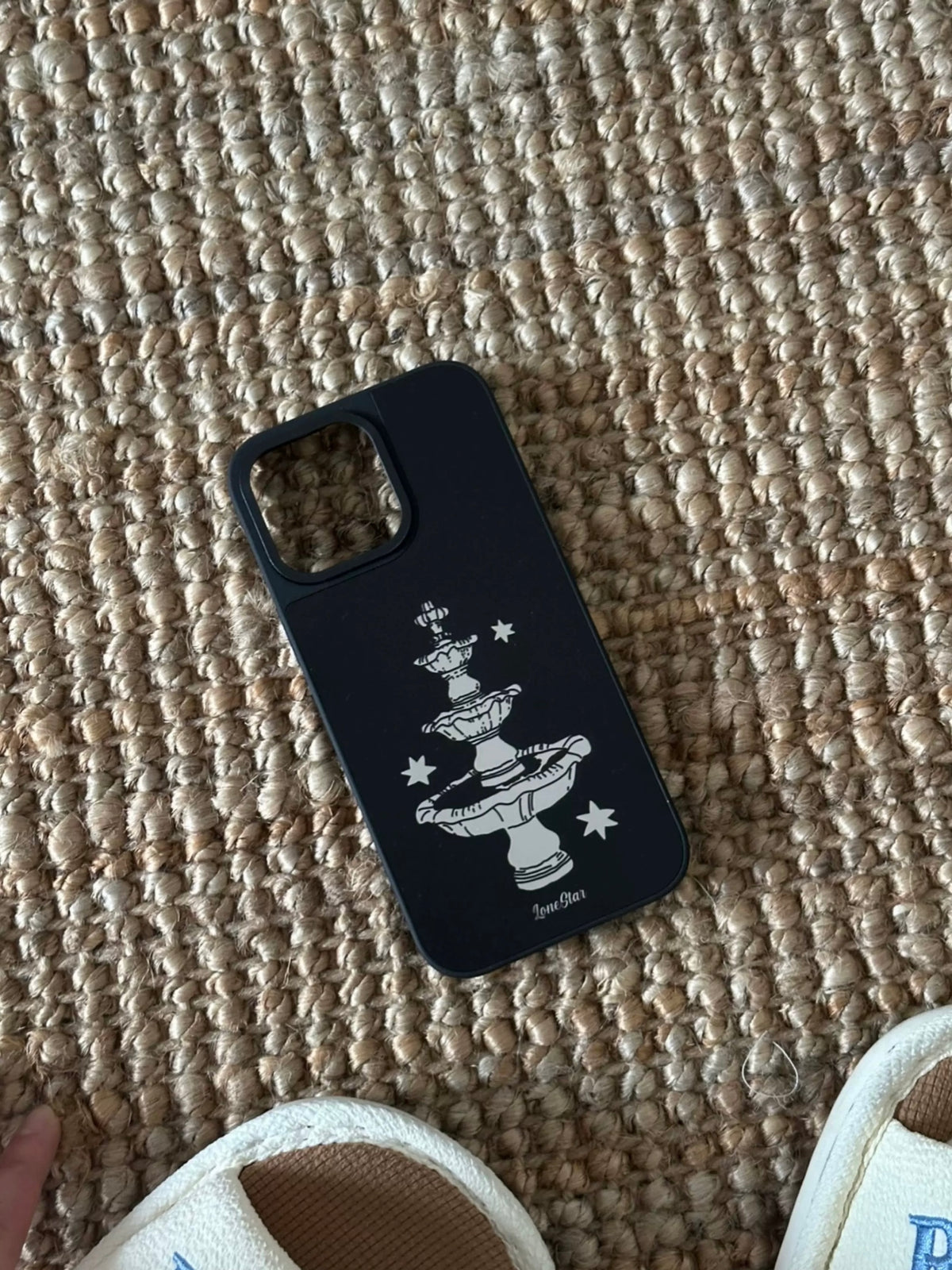 A black mirror phone case with a pale tiered fountain and stars, shown lying at an angle.