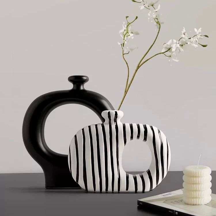 Black and white striped vase with a black vase and candle on a gray surface.