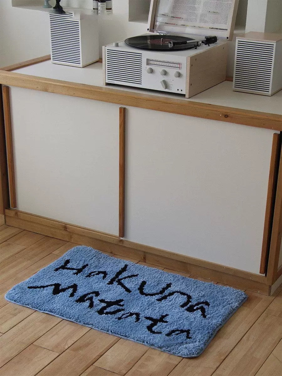 A blue bath mat with black handwriting is shown in front of a kitchen cabinet in a wider room view.