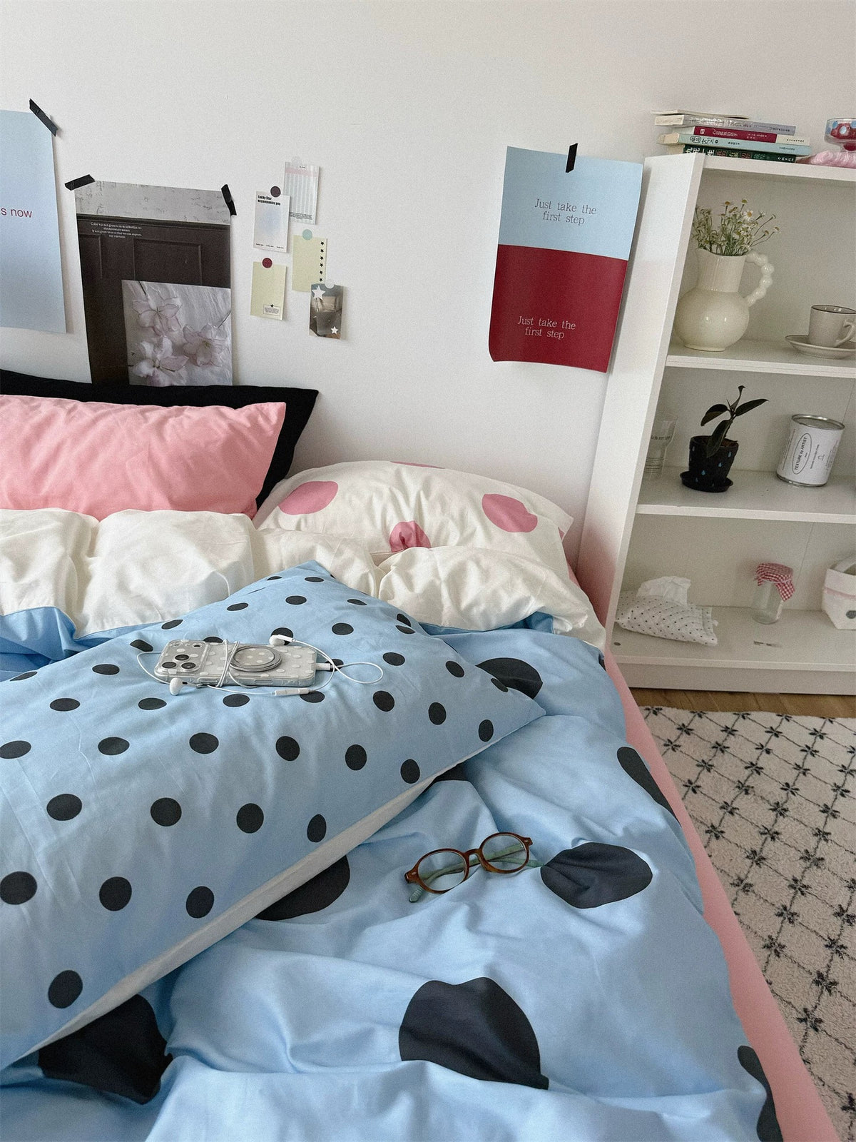 A folded section of blue bedding shows small black dots beside the larger dot pattern, with pink and cream pillows behind.