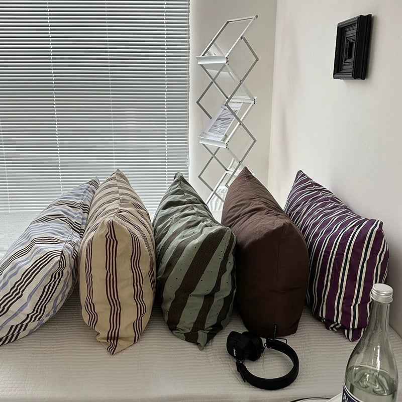 Colorful striped pillows on a window sill with a bottle and remote control.