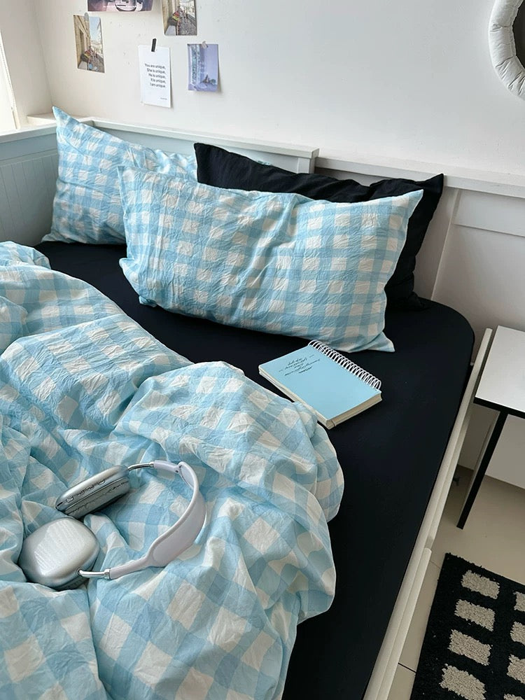 Bed with blue checkered bedding and pillows, next to a small table.