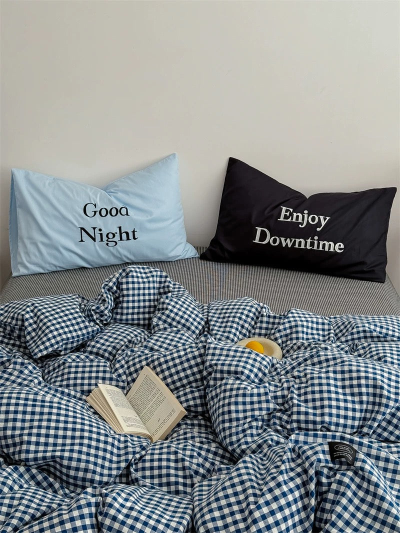 Bed with checkered duvet, 'Good Night' and 'Enjoy Downtime' pillows.