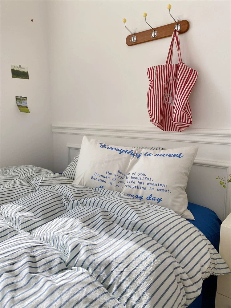 Bedroom with striped bedding and a pillow with text, red and white bag hanging on wall.
