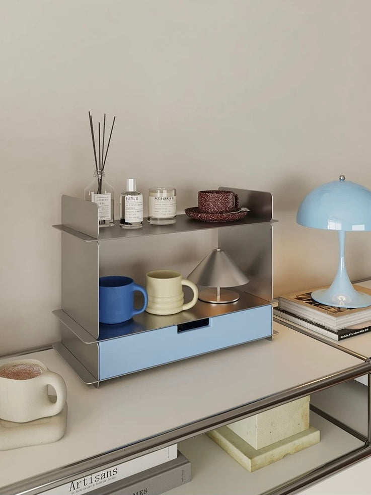 Blue desk shelf with two levels, colorful mugs and a silver cone lamp on a console table