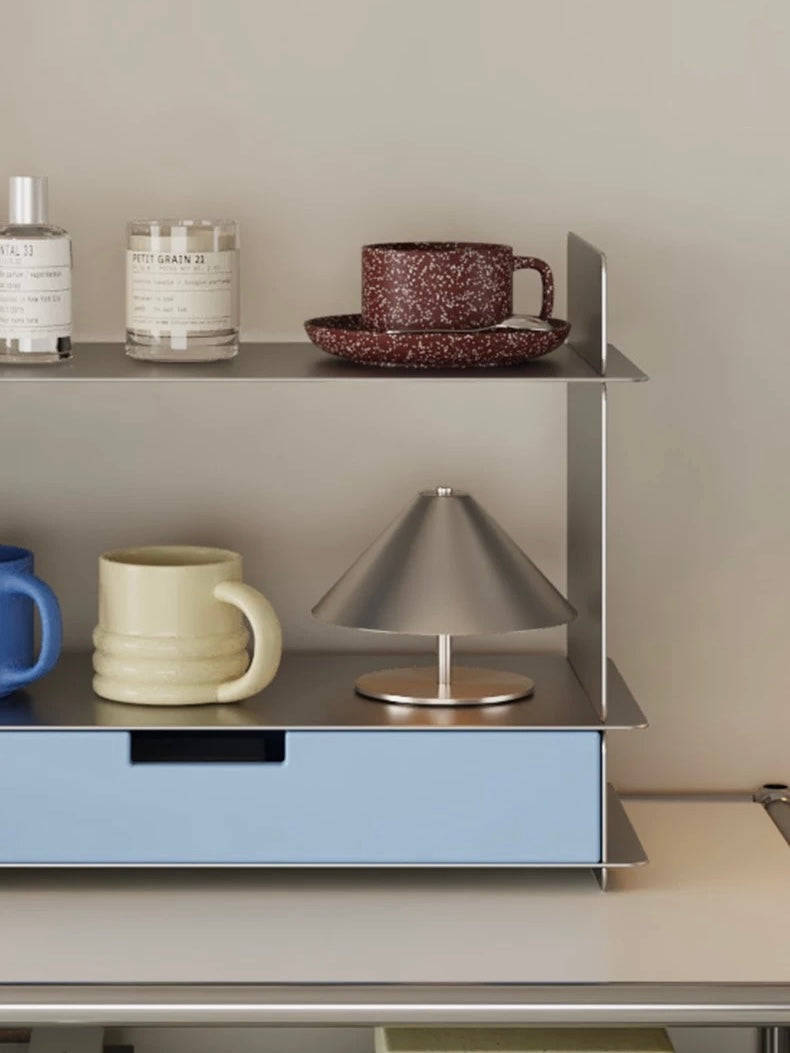 Close up of the blue drawer front with two mugs and a silver cone lamp on the steel shelf