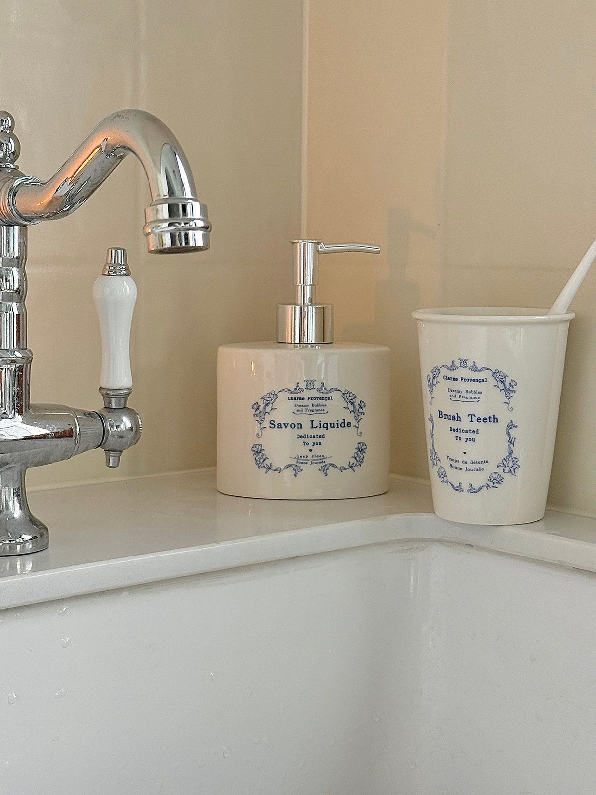 A blue floral soap dispenser stands beside a matching toothbrush cup on the edge of a bathroom sink.